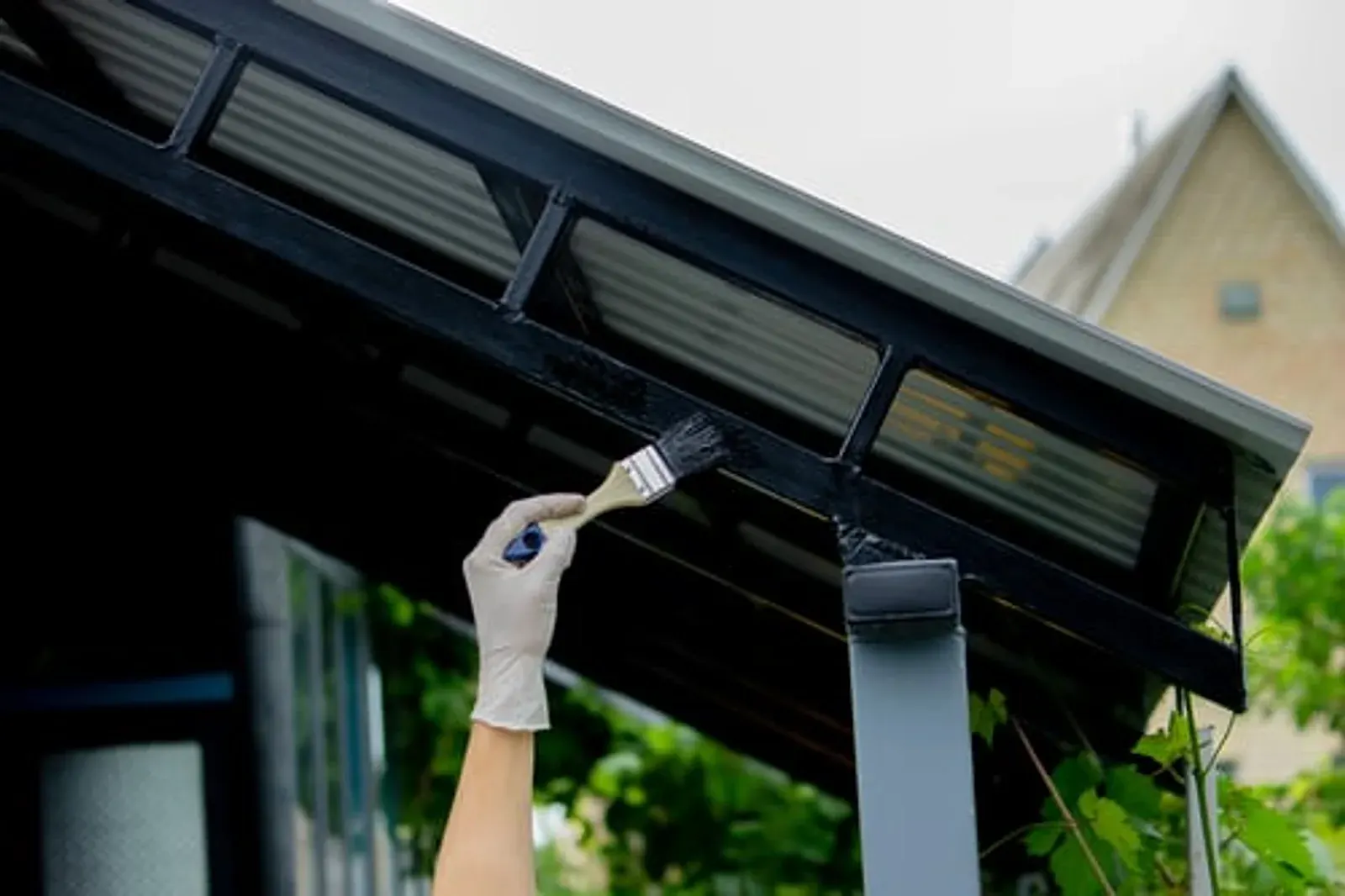 Painter's gloved hand carefully brushing paint onto exterior trim