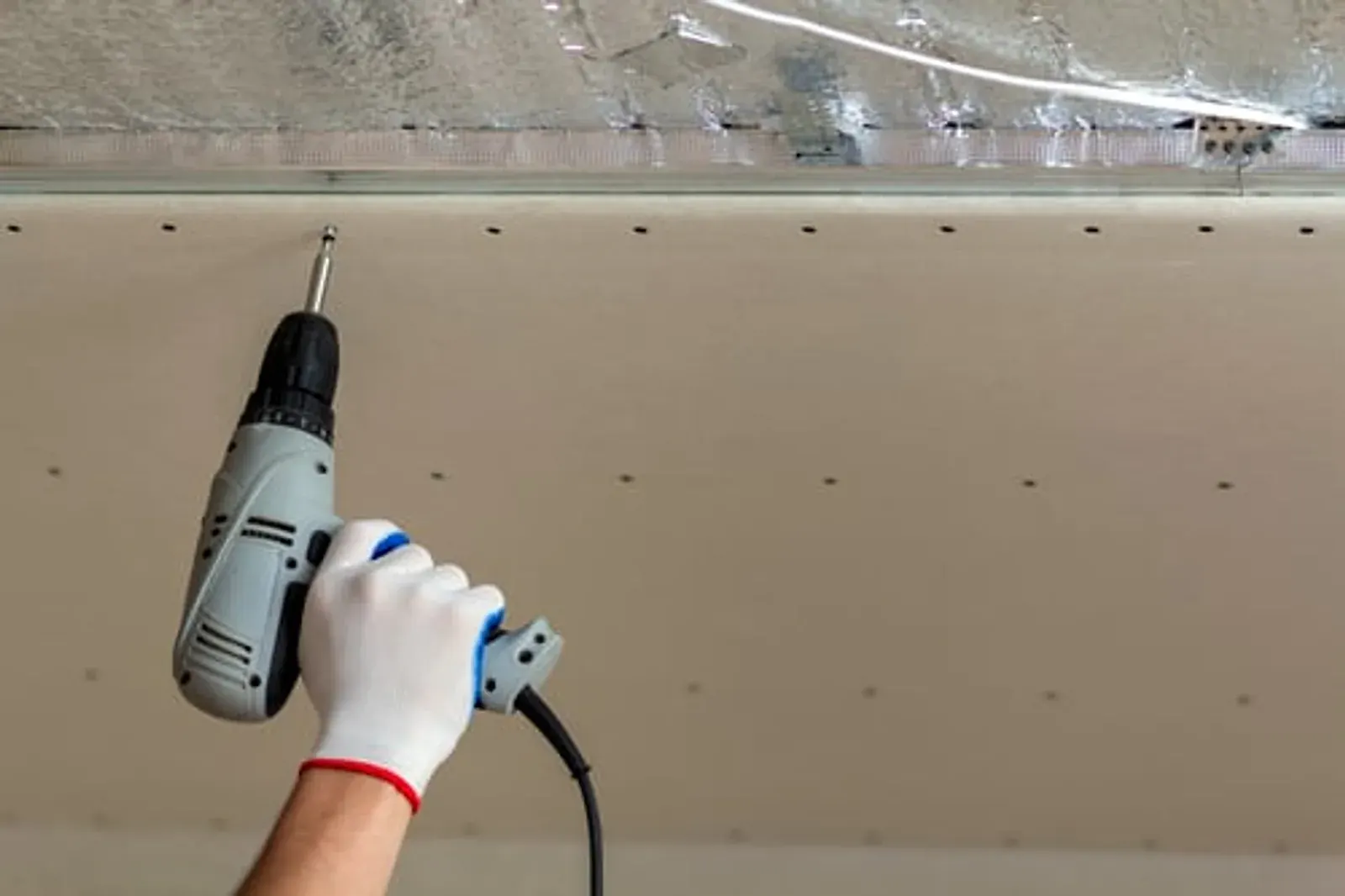 Worker fixing a sheet of drywall to a wall frame with a screw gun