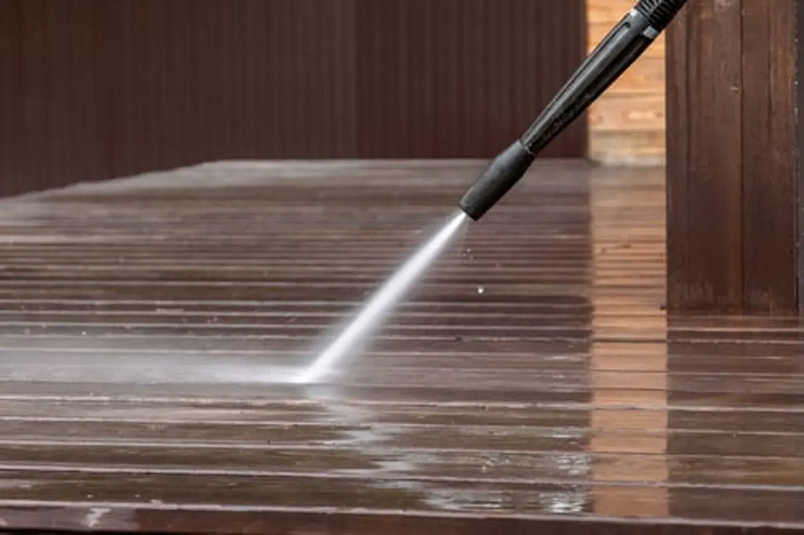 Pressure washer cleaning a wooden deck surface with a strong water jet