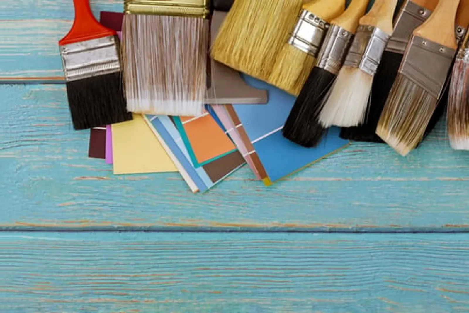 Assorted paint brushes and colour swatches laid out on a painted wooden surface