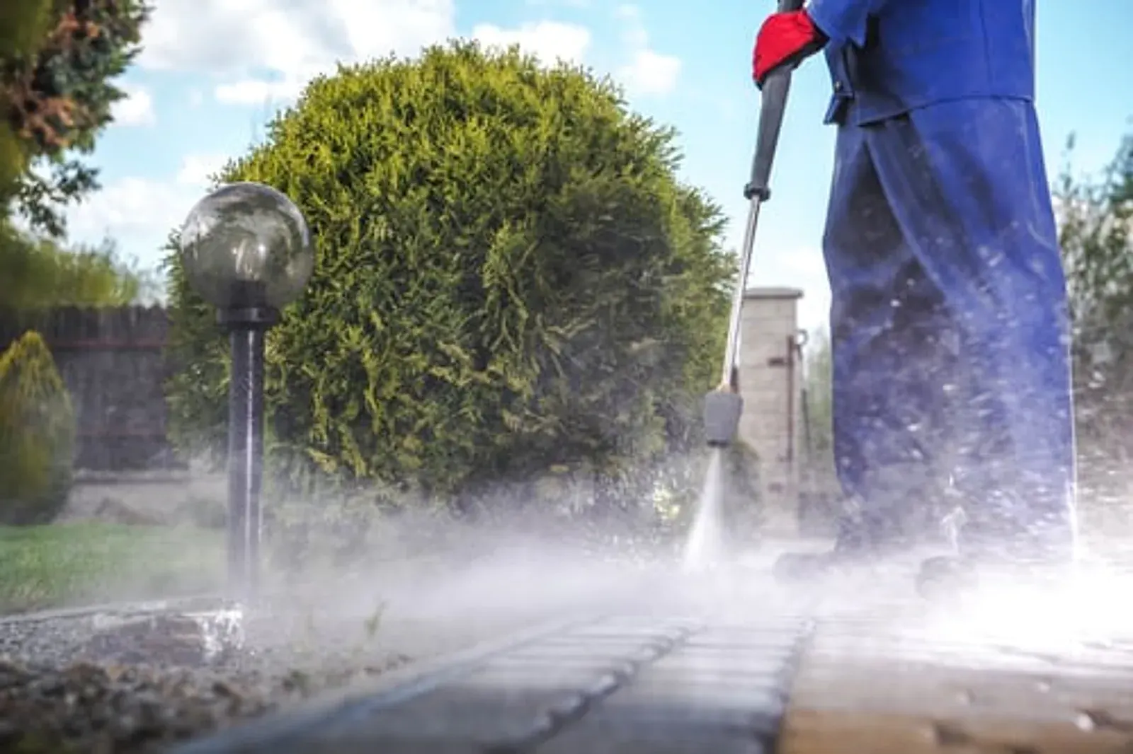 Technician pressure washing an exterior walkway alongside landscaped garden beds